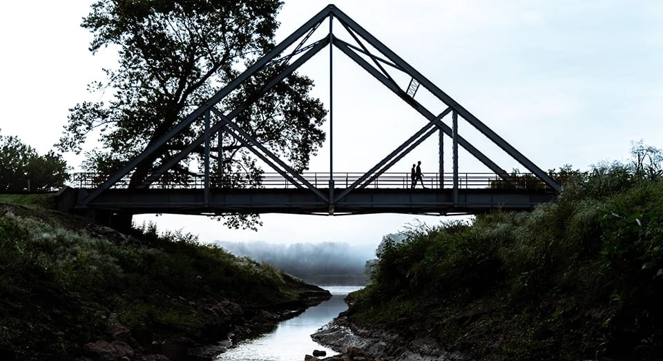 Two people walk together across a foggy bridge.